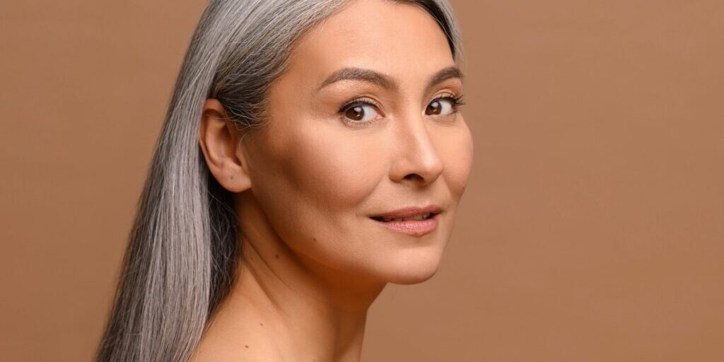 Headshot beautiful middle-aged Asian woman with fresh clean healthy skin isolated on beige